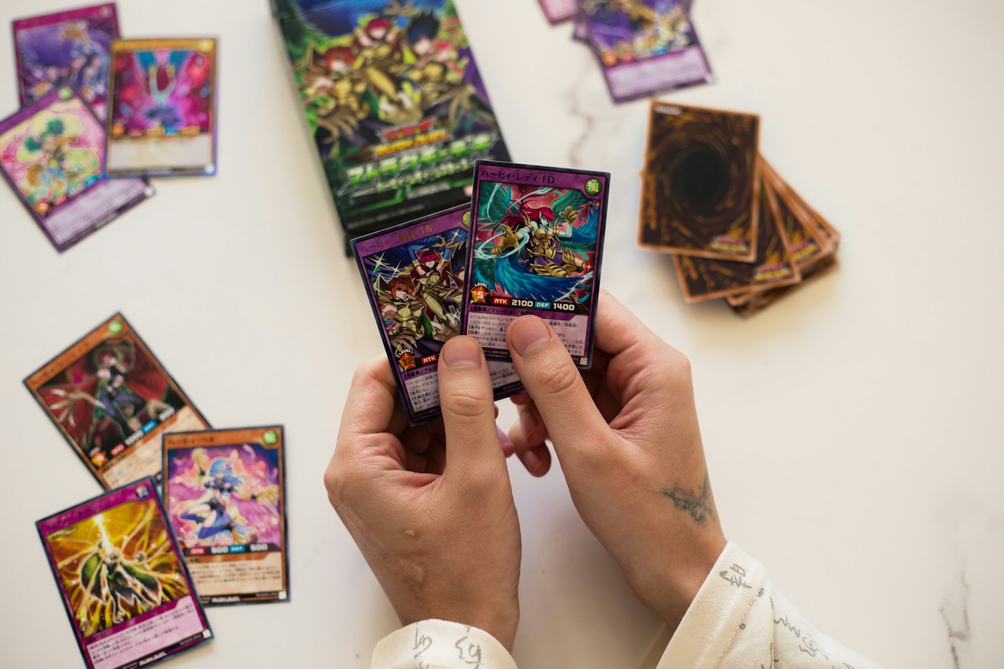 Mains tenant des cartes à collectionner d'anime avec un paquet de boosters à proximité.